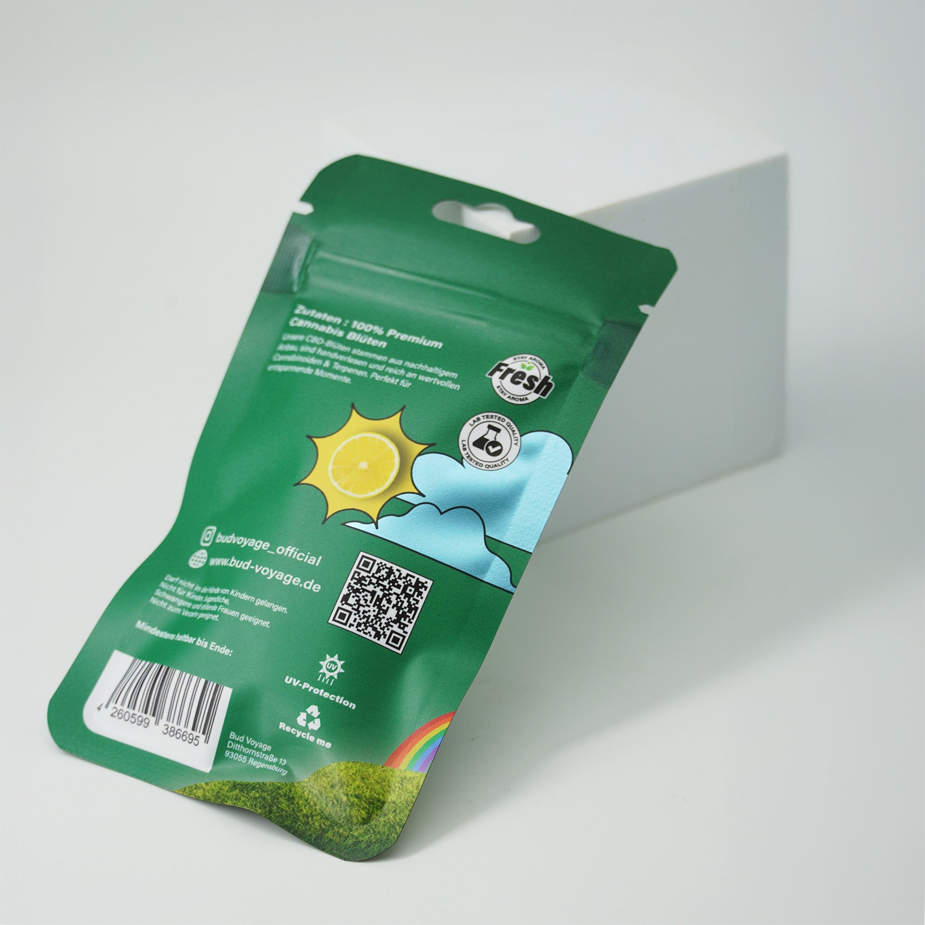 Bud Voyage Produktverpackung zeigt eine sonnige Zitronenscheibe, Regenbogen und QR-Code auf grünem Hintergrund mit UV-Schutz und Recyclinghinweis