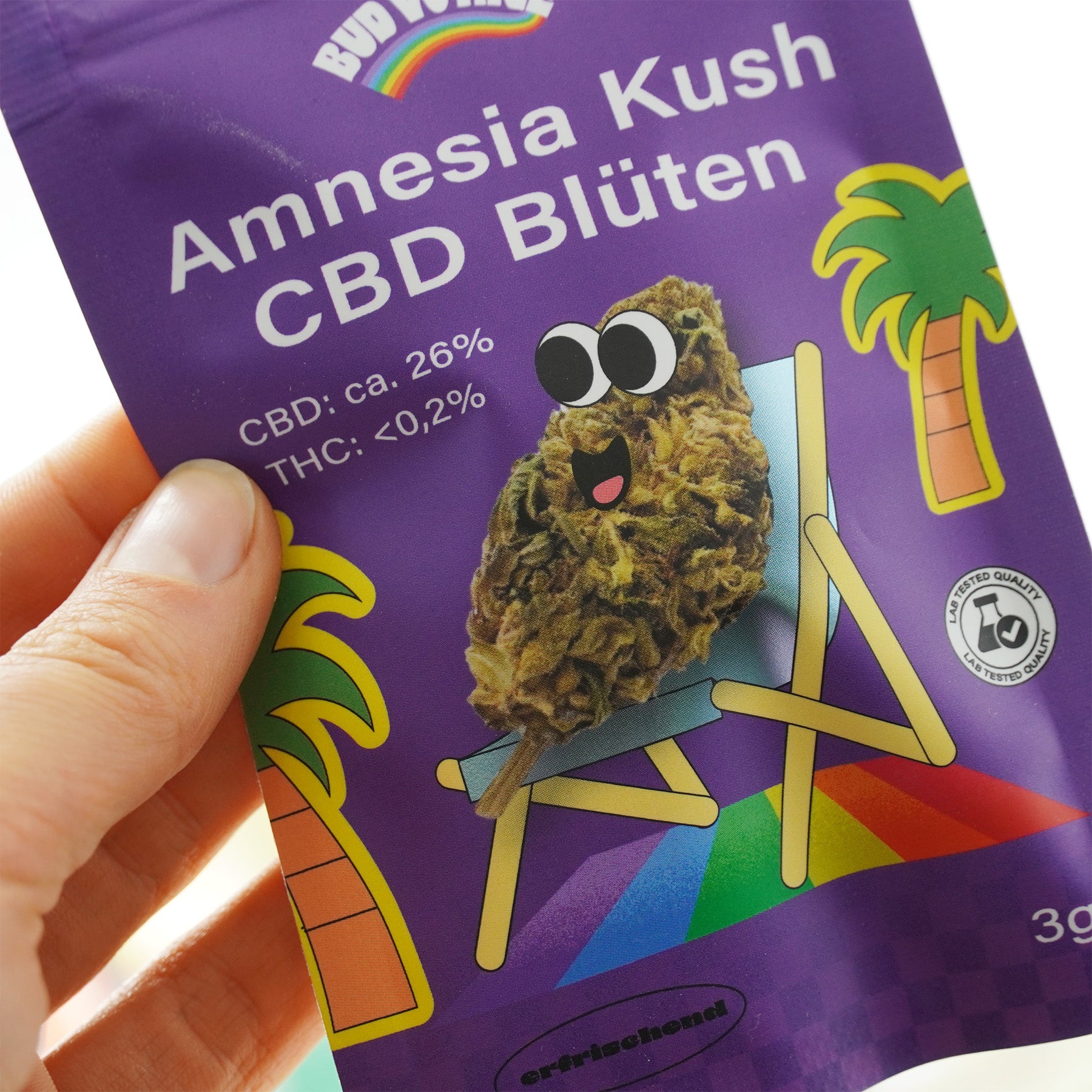 Bud World Amnesia Kush CBD Blüten Verpackung zeigt einen Cartoon-Hanfblüten-Charakter auf einem Liegestuhl vor Palmen mit einem Regenbogen und einem Qualitätssiegel
