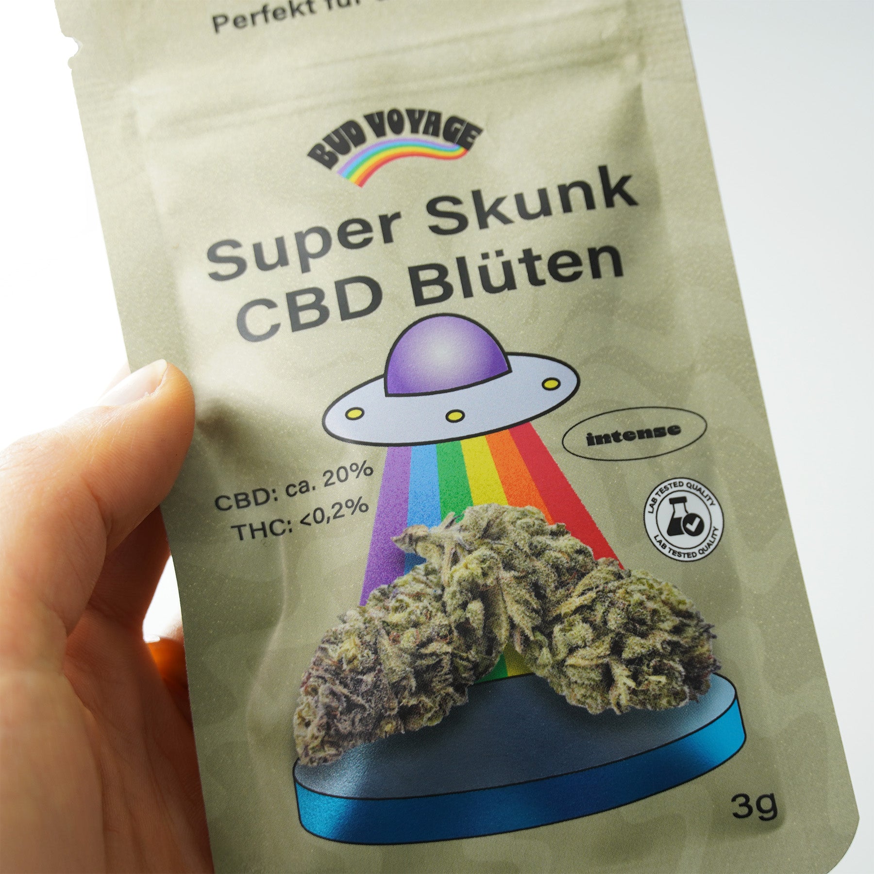 Bud Voyage Verpackung zeigt Super Skunk CBD Blüten mit einem UFO, Regenbogen und leuchtend blauen Podest, 3g Packung
